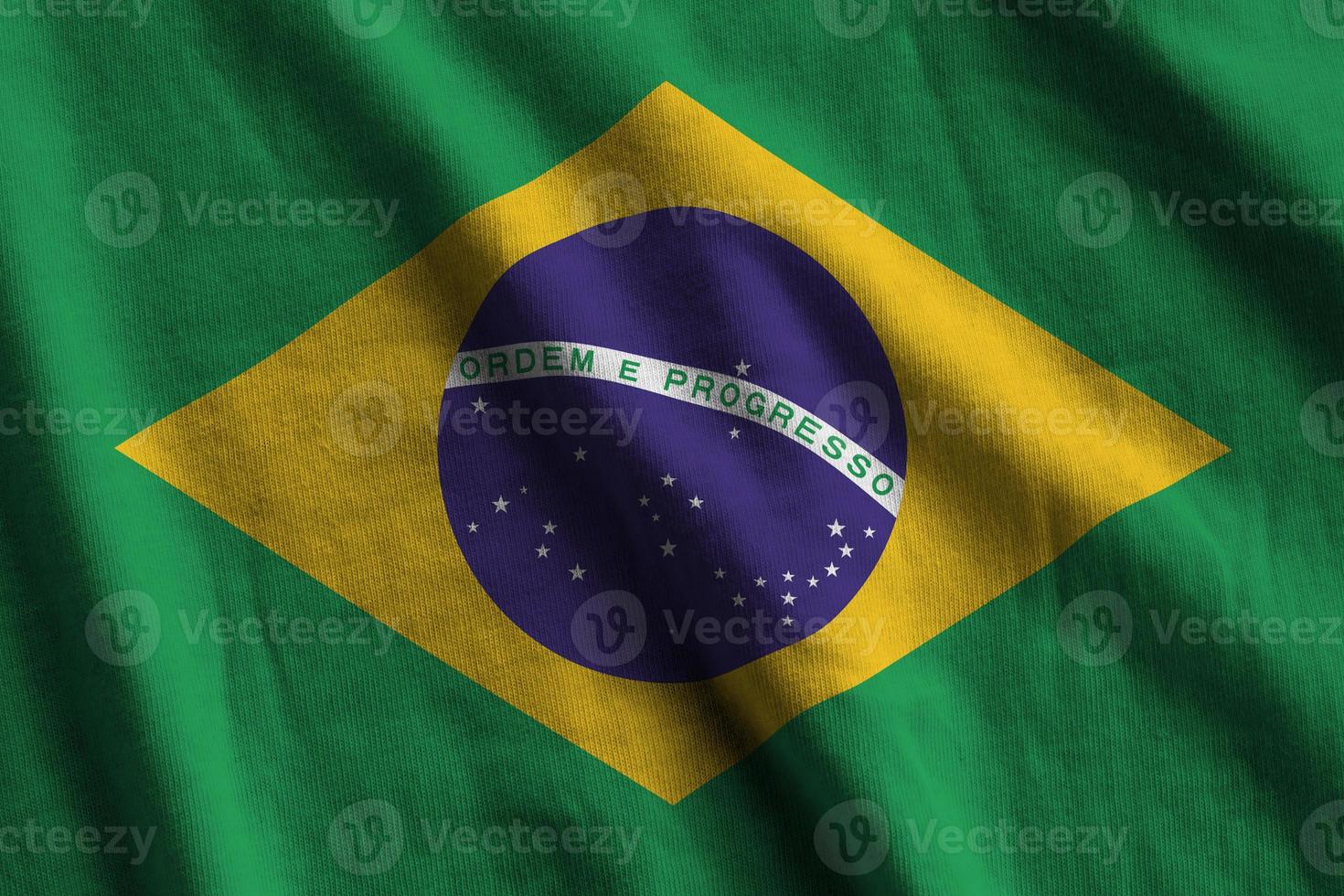 bandera de brasil con grandes pliegues ondeando de cerca bajo la luz del estudio en el interior. los símbolos y colores oficiales en banner foto