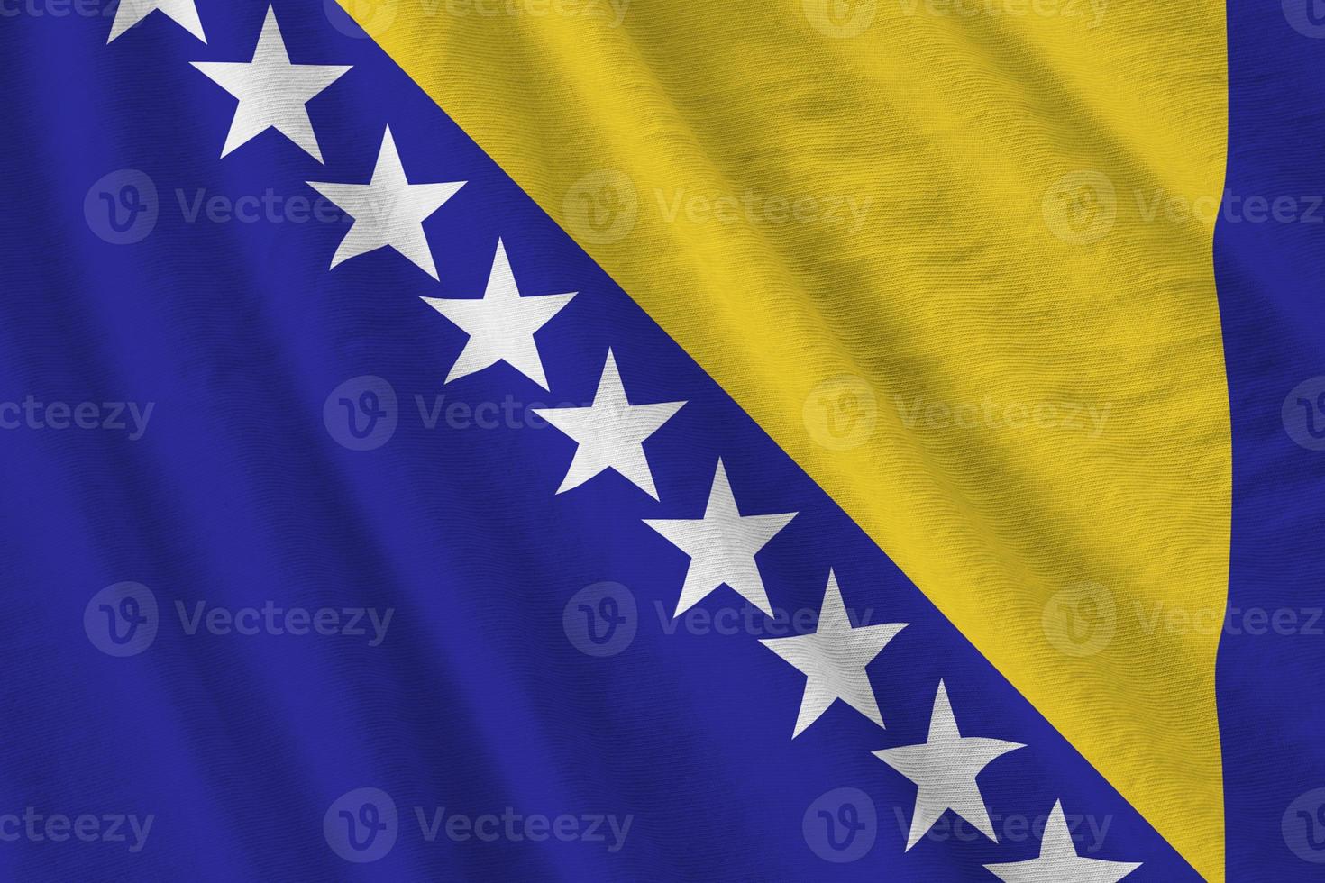 Bosnia and Herzegovina flag with big folds waving close up under the studio light indoors. The official symbols and colors in banner photo