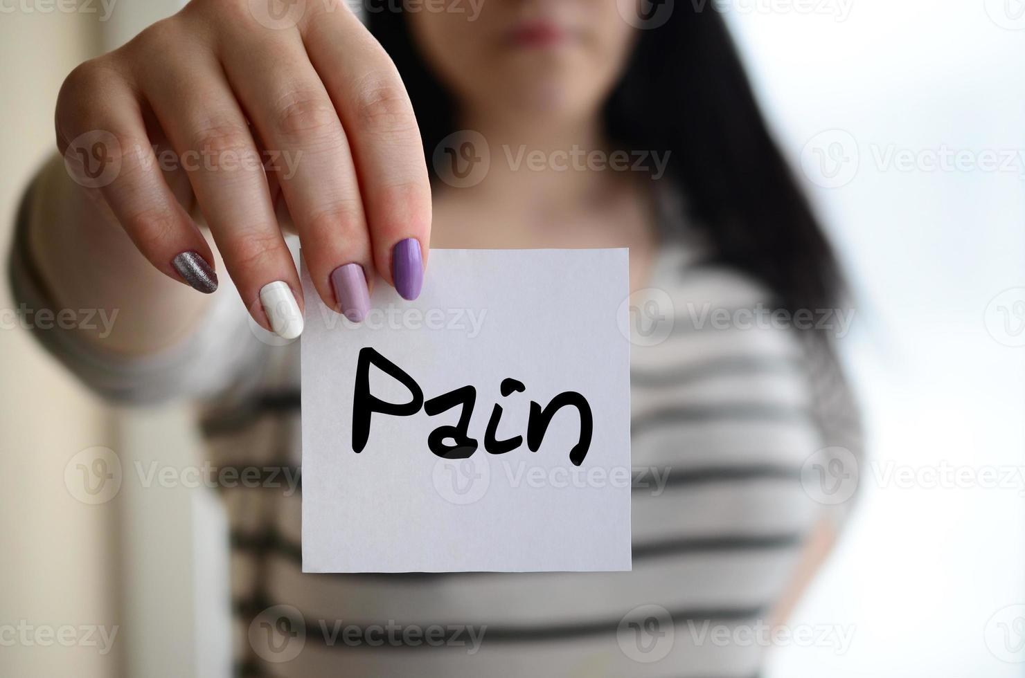 Young sad girl shows a white sticker. Caucasian brunette holding a sheet of paper with message. Pain photo