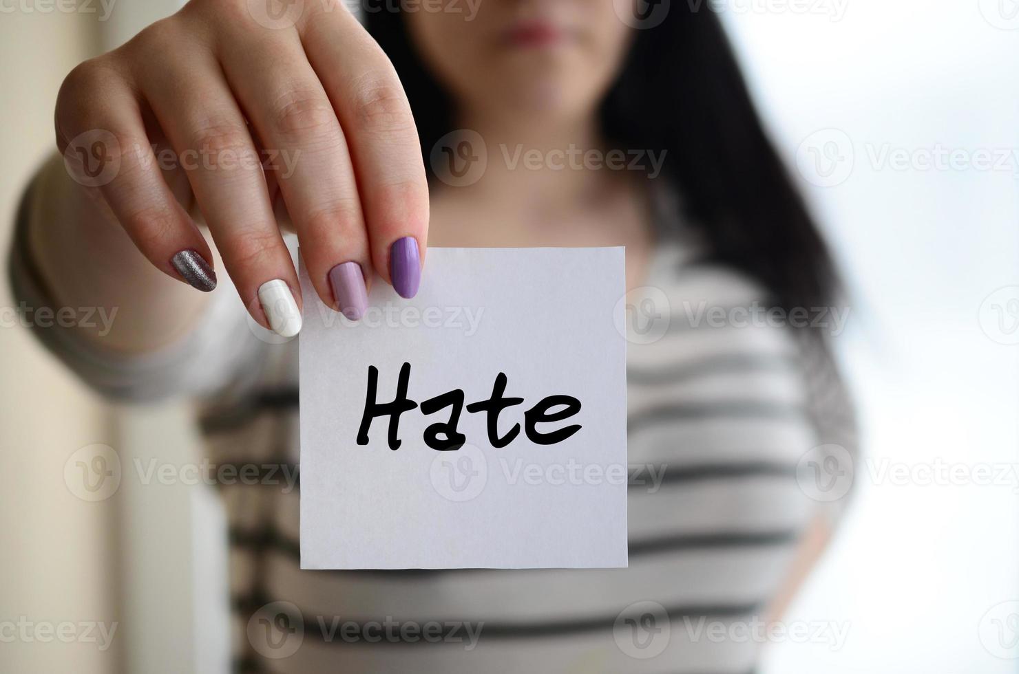 Young sad girl shows a white sticker. Caucasian brunette holding a sheet of paper with message. Hate photo