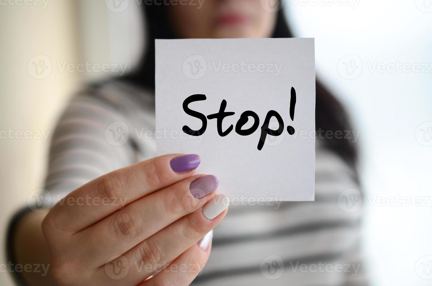 Young sad girl shows a white sticker. Caucasian brunette holding a sheet of paper with message. Stop photo