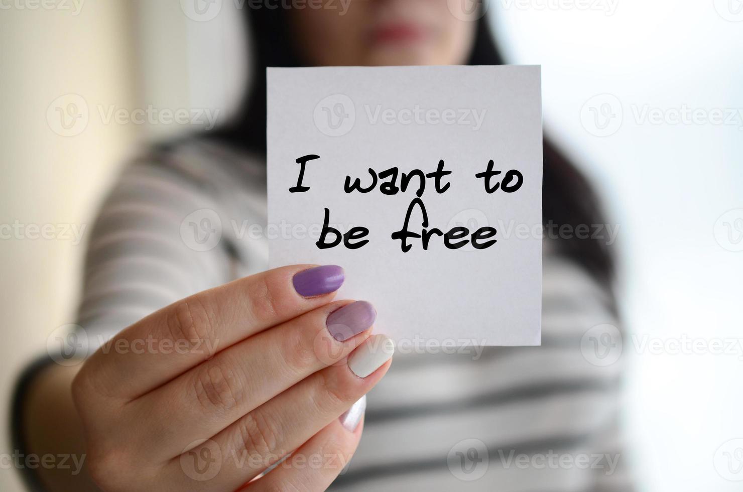 Young sad girl shows a white sticker. Caucasian brunette holding a sheet of paper with message. I want to be free photo