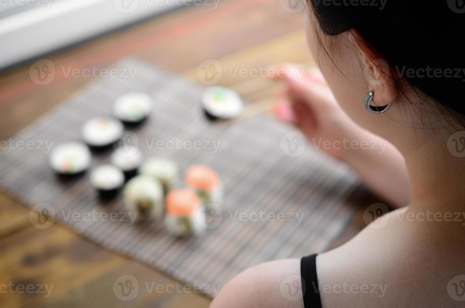 Brunette girl with chopsticks holds a sushi roll on a bamboo straw serwing mat background. Traditional Asian food photo