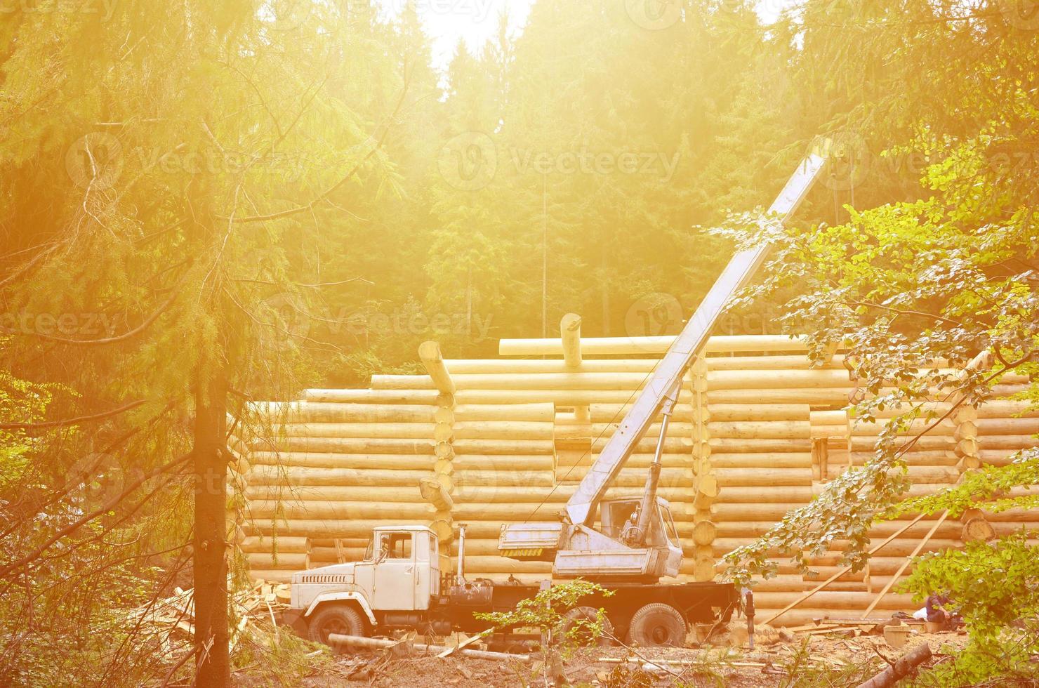 el proceso de construcción de una casa de madera a partir de vigas de madera de forma cilíndrica. grúa en condiciones de trabajo foto