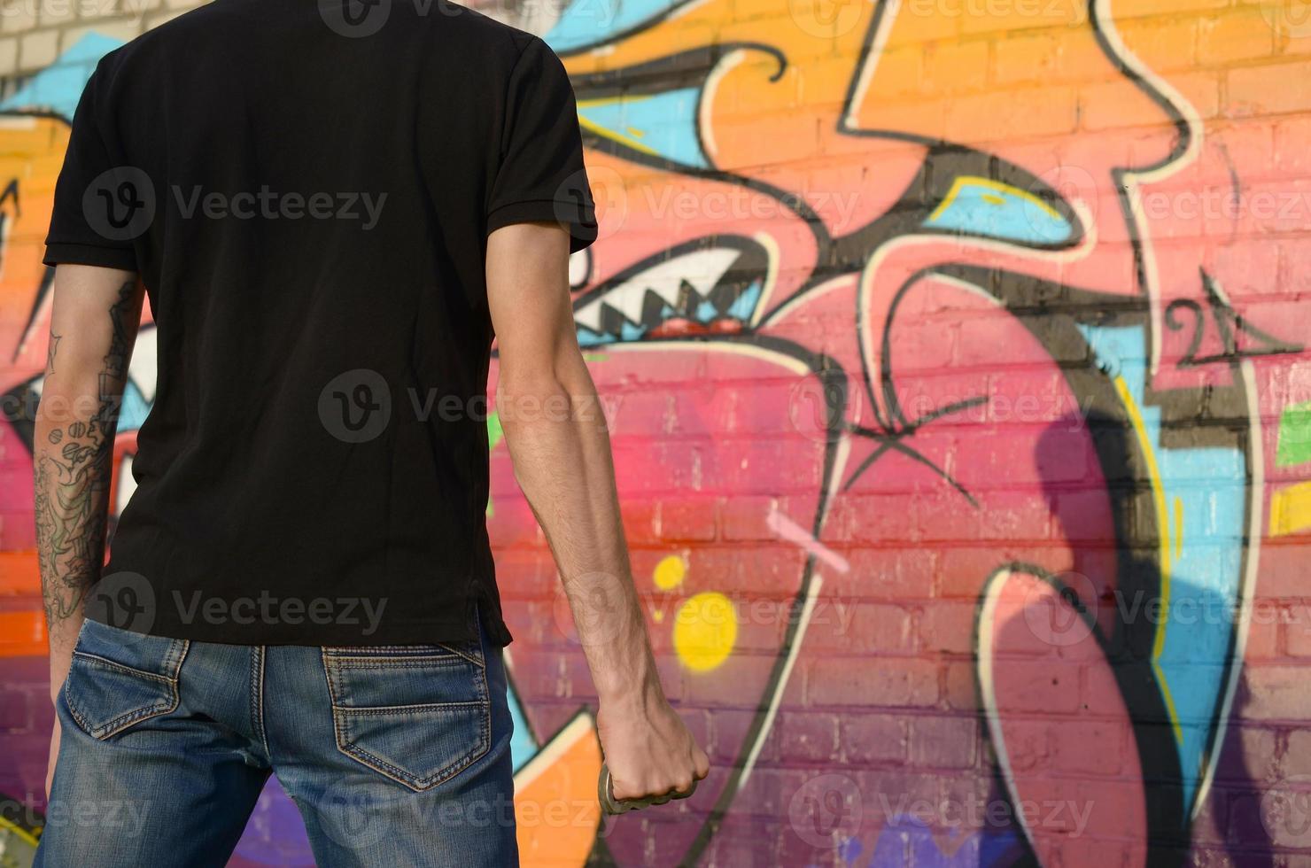 Back view of young caucasian man with brass cnuckle on his hand against ghetto brick wall with graffiti paintings. Concept of criminal forces and aggression charge photo