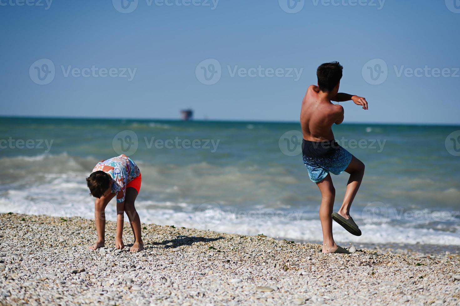 dos hermanos arrojan guijarros al mar en la playa de porto sant elpidio, italia. foto