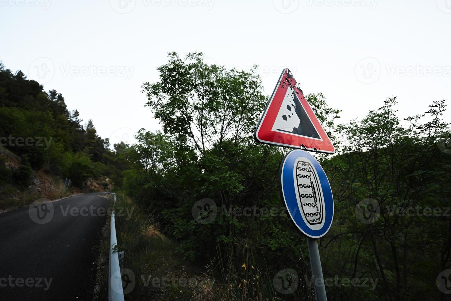 Road sign falling stones, traffic sign caution possible falling rocks with compulsory snow chains aboard car in winter. photo