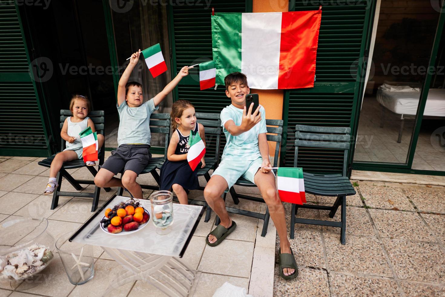 Happy four kids with italian flags celebrating Republic Day of Italy. Boy making selfie on phone. photo