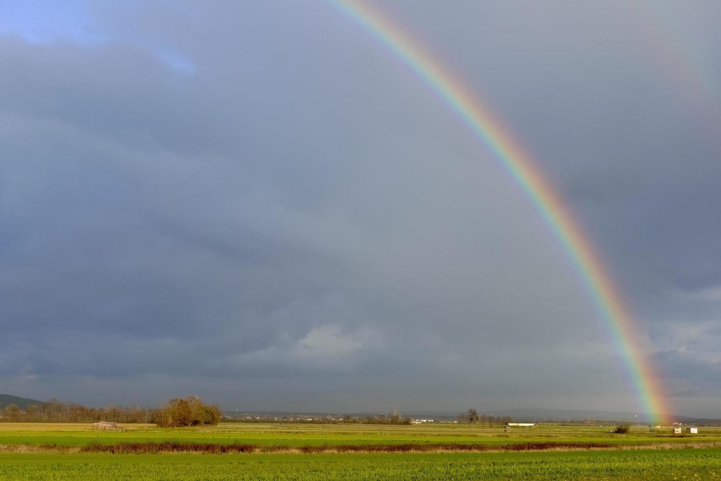 arco iris sobre nubes de lluvia oscuras sobre campos verdes en un paisaje plano foto