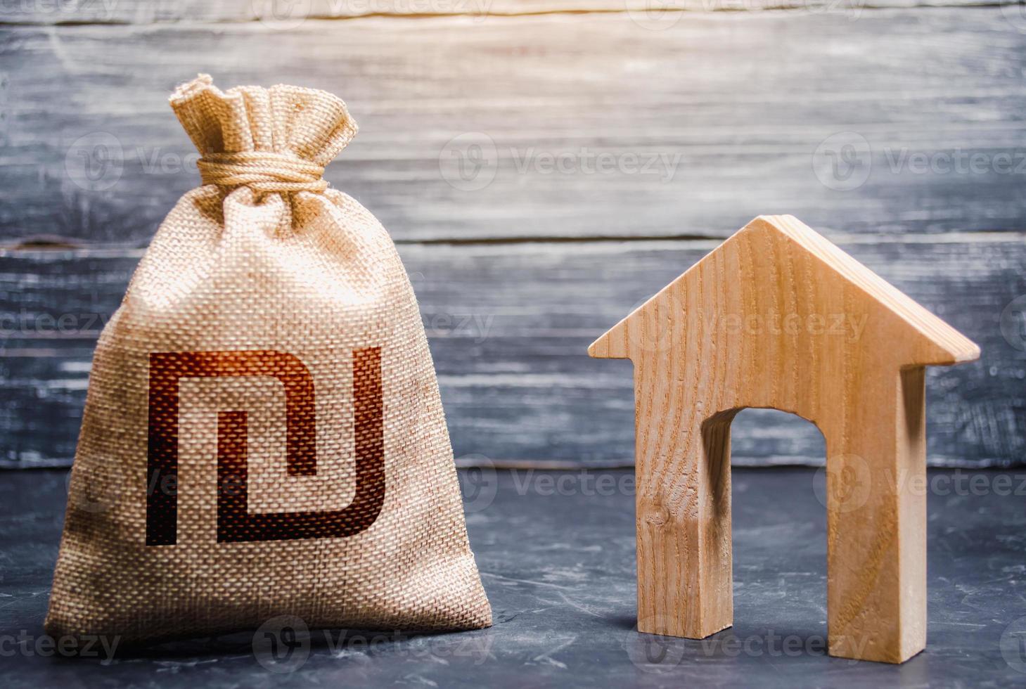 Wooden house and a israeli shekel money bag. Home purchase, investment in real estate construction. House project development. Realtor services. Generating income through rent or sale. Mortgage loan. photo