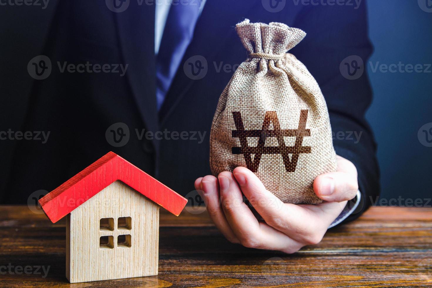 Man holds out a south korean won bag near the house. Bank approval for a mortgage loan. Property appraisal. Favorable terms and conditions, low interest rate. Home purchase, invest in real estate. photo