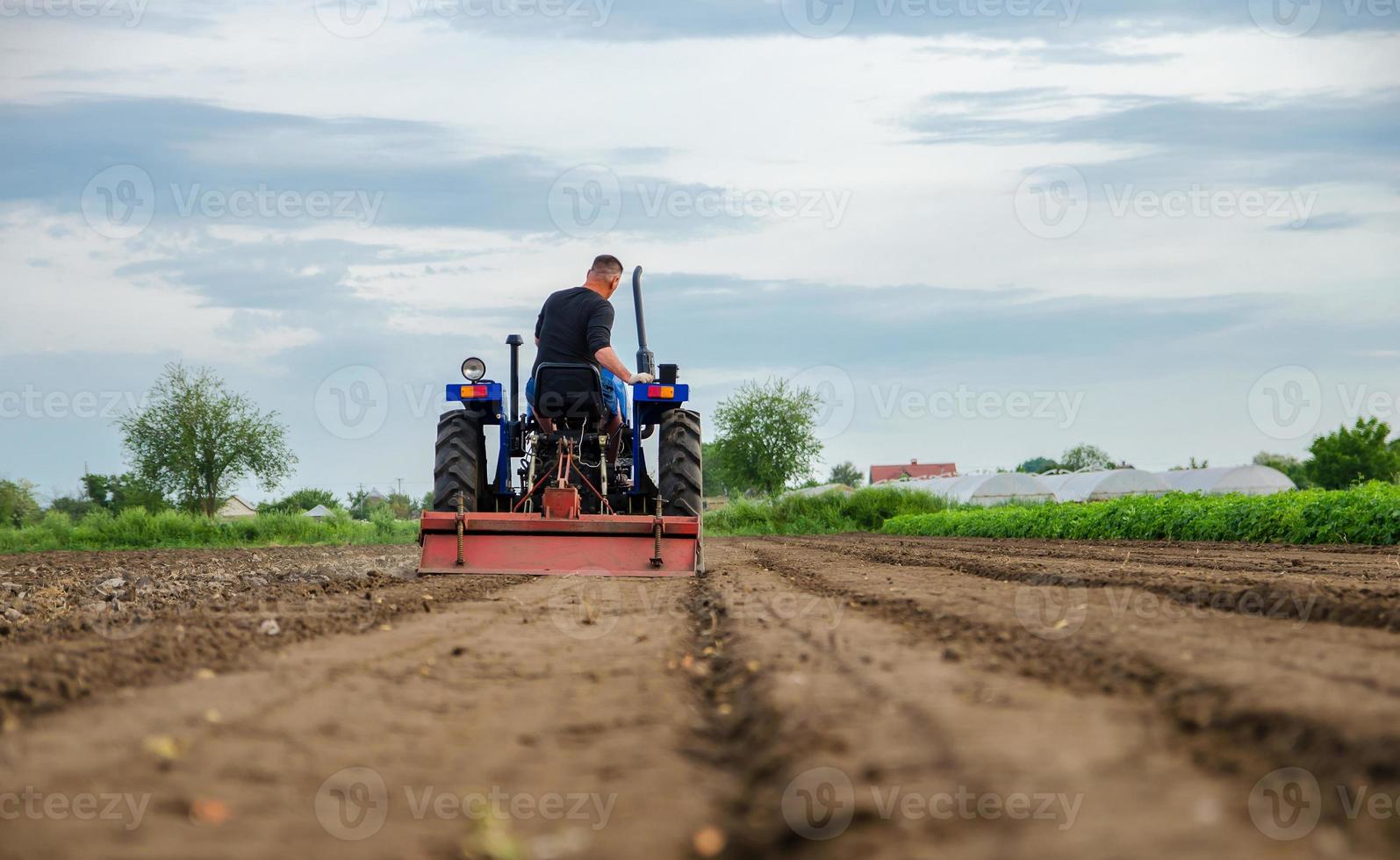 A farmer drives a tractor and cultivates an agricultural field. Milling soil, crushing before cutting rows. Farming, agriculture. Loosening surface, land cultivation. Plowing field. photo