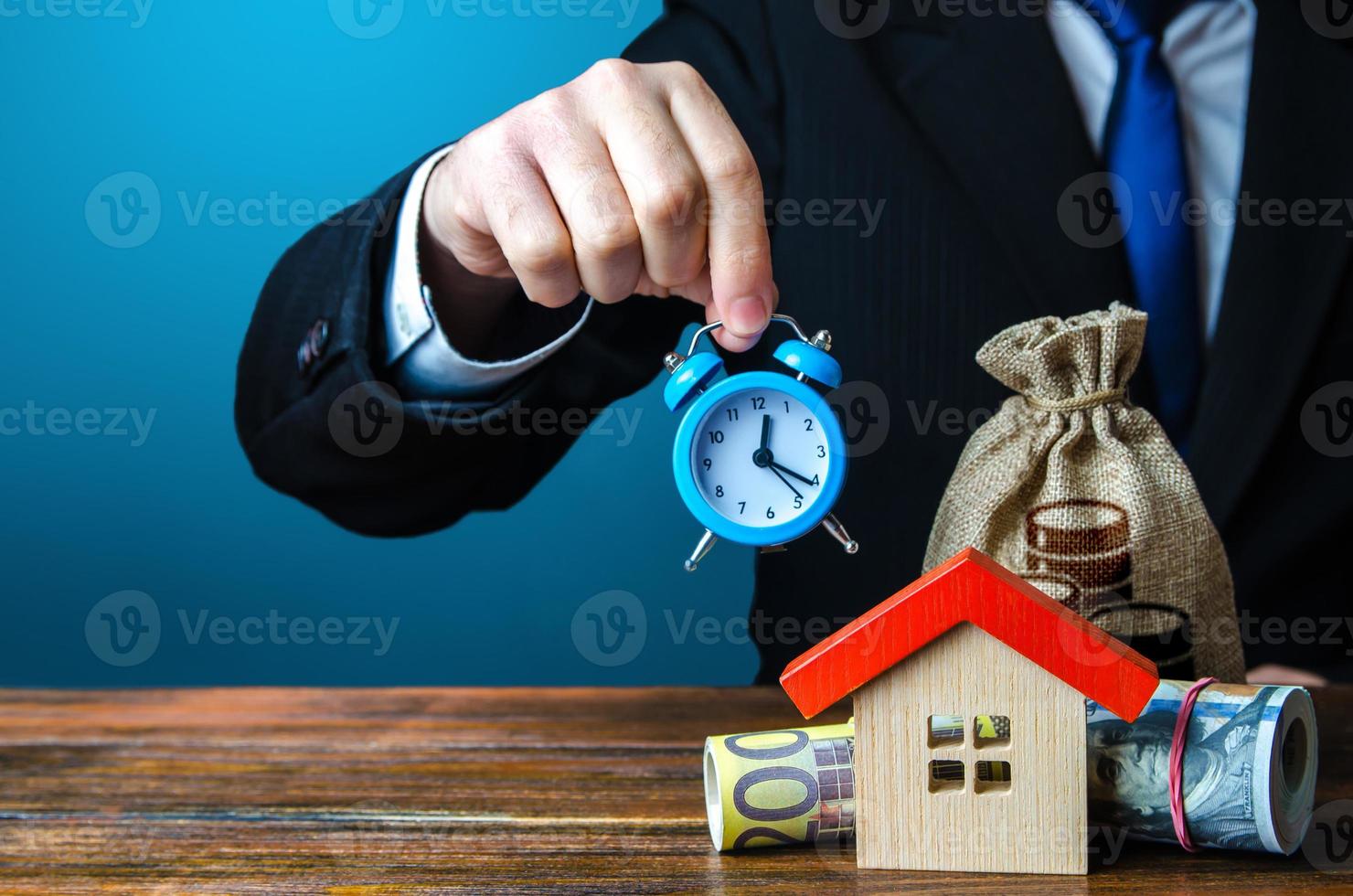 A man holds an alarm clock over the house and money. Limited offer