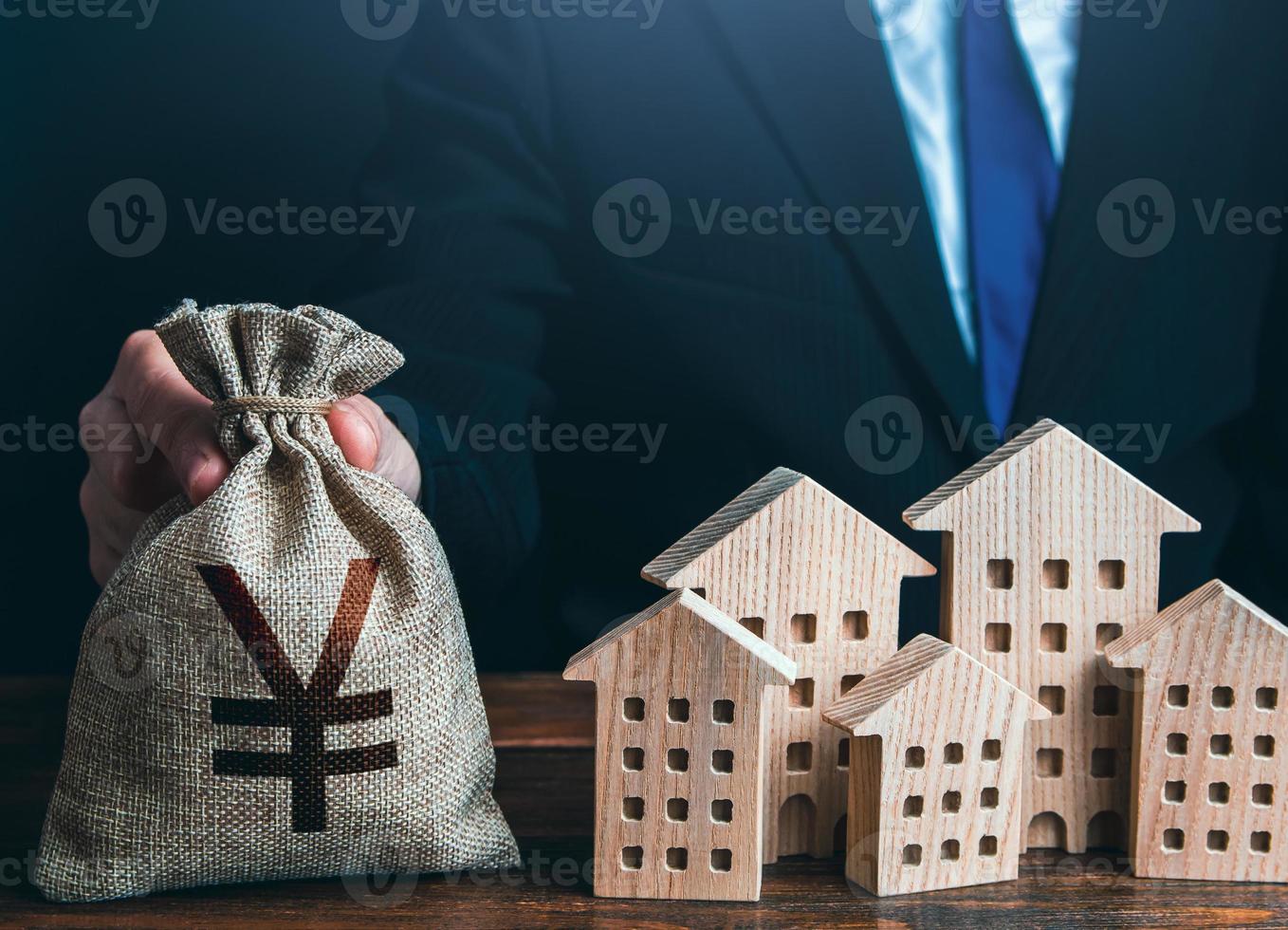 A businessman puts a yuan or yen money bag near the houses. Construction industry, rental business and hotel tourism. Municipal budget of the city. Official. Investments in real estate assets. photo