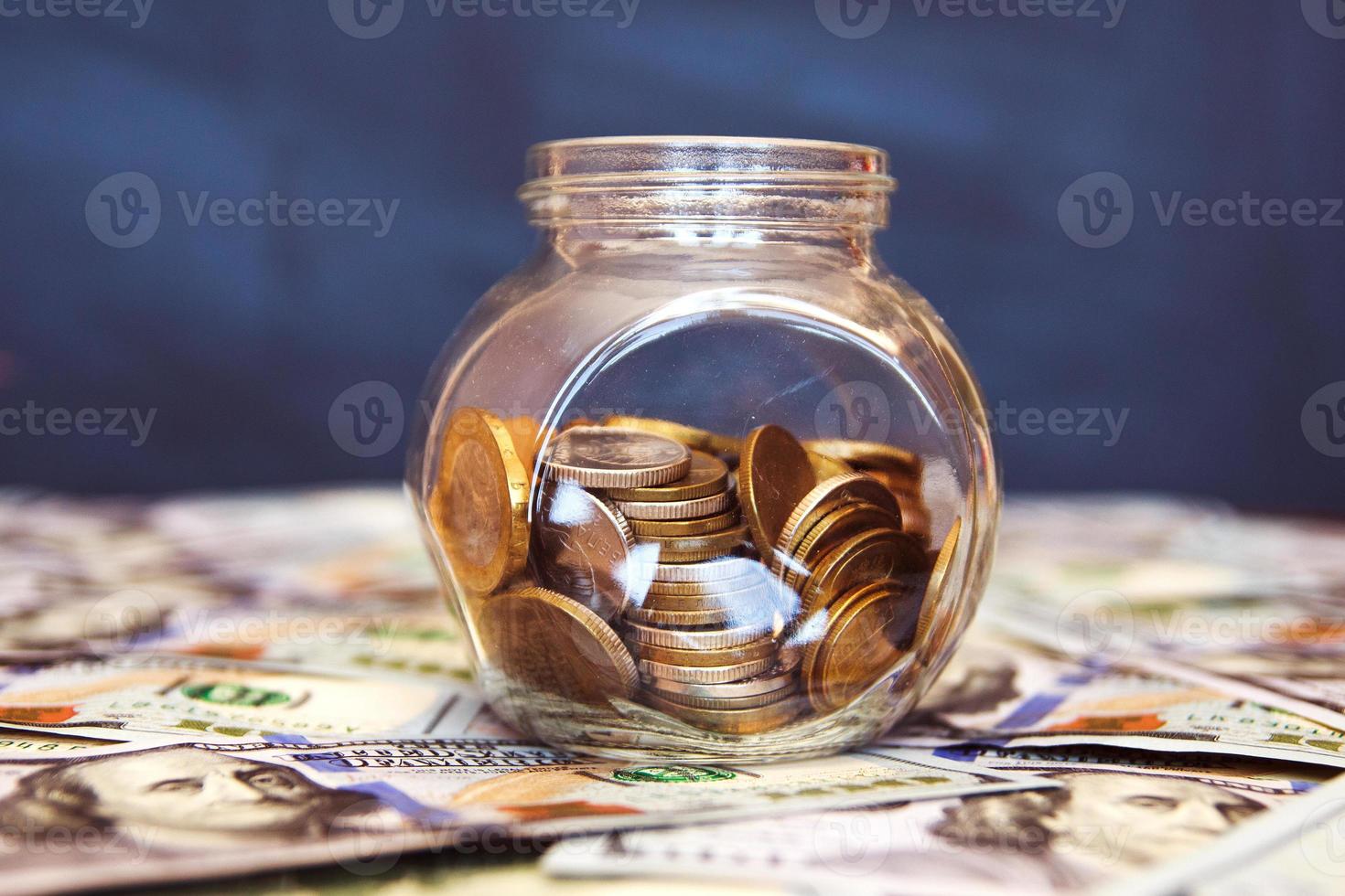 Glass jar with coins on the black background. A lot of dollar bills photo