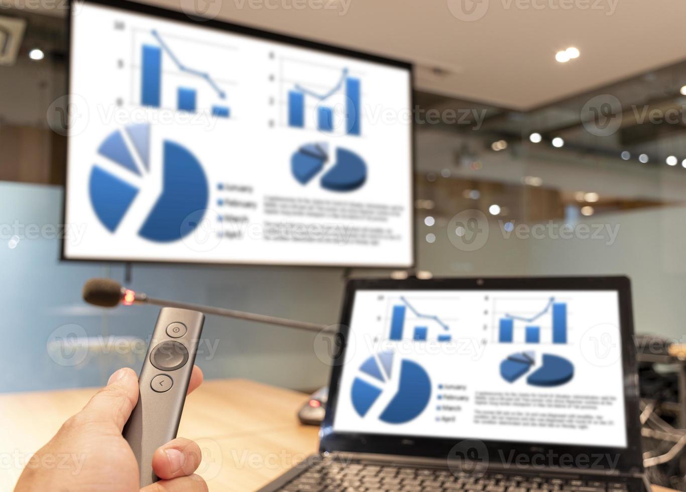 Businessman hand hold remote control slide with presentation on display projector screen and laptop photo