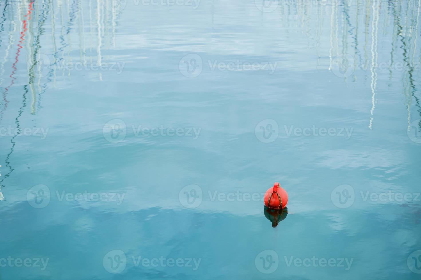 Orange buoy floating on the waves of the sea surface in the bay. Reflection of yacht masts in the water. The concept of the safety of human life. photo