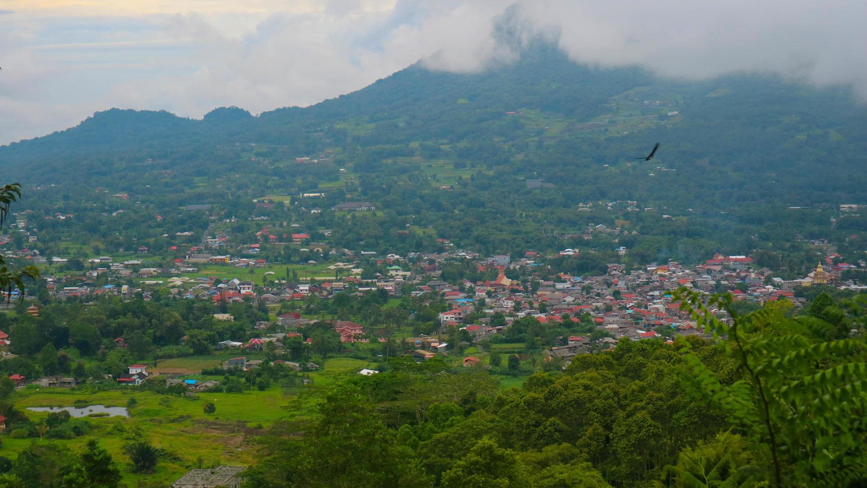 la vista del cielo nublado, árboles, montañas y casas fue fotografiada desde arriba de la colina foto