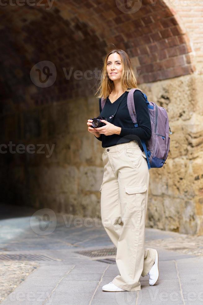 Confident female photographer standing near aged archway during trip photo