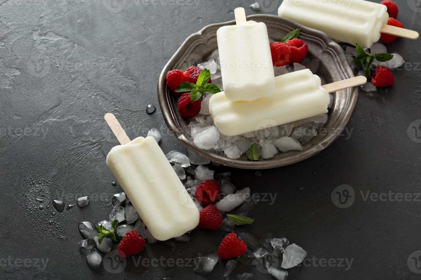 Coconut popsicles with raspberries on black background photo