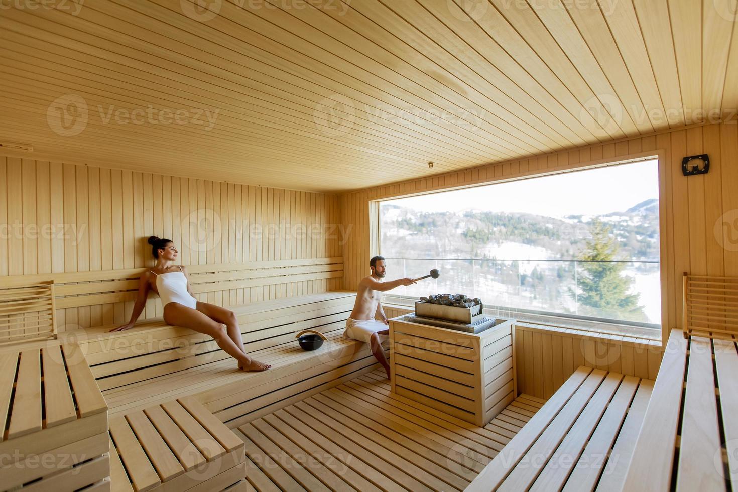 pareja joven relajándose en la sauna y viendo el bosque de invierno a través de la ventana foto