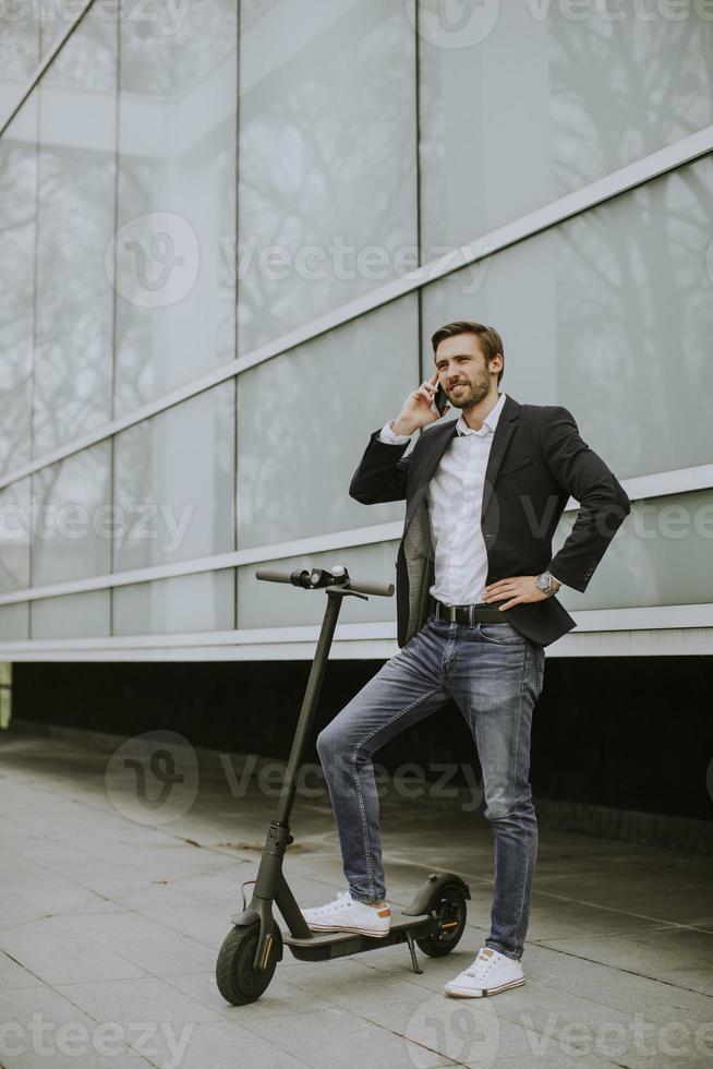 Young businessman using mobile phone  on electric scooter photo