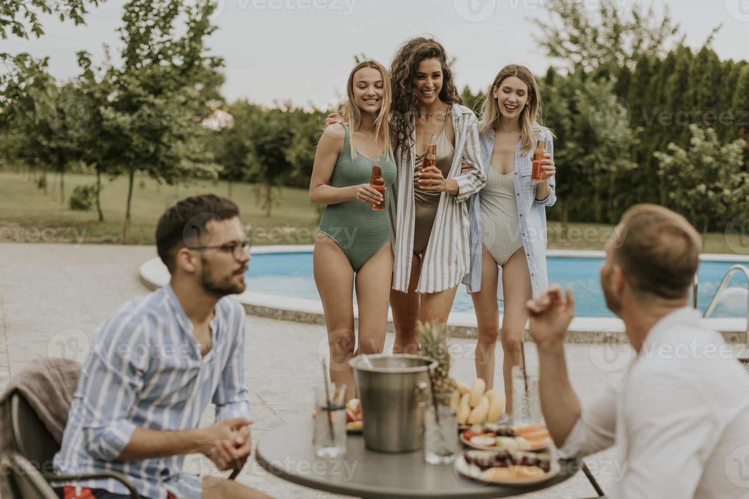 Group of young people cheering with drinks and eating fruits by the pool in the garden photo