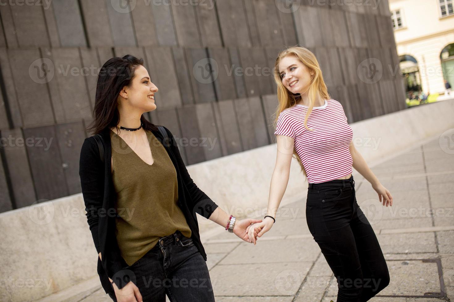 dos mujeres jóvenes caminando por la calle y tomándose de la mano foto