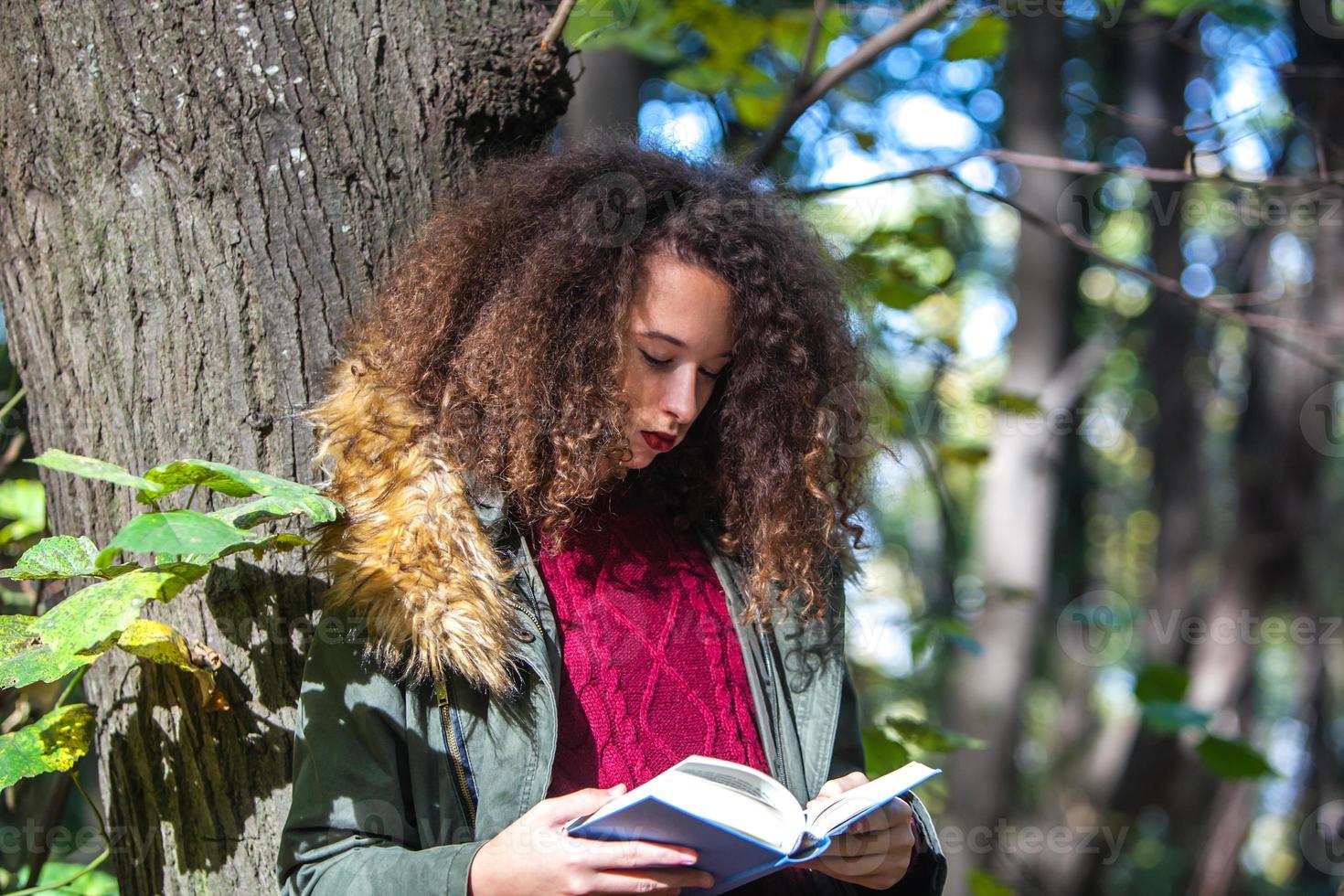 Curly hair teen girl reading book in autumn park photo