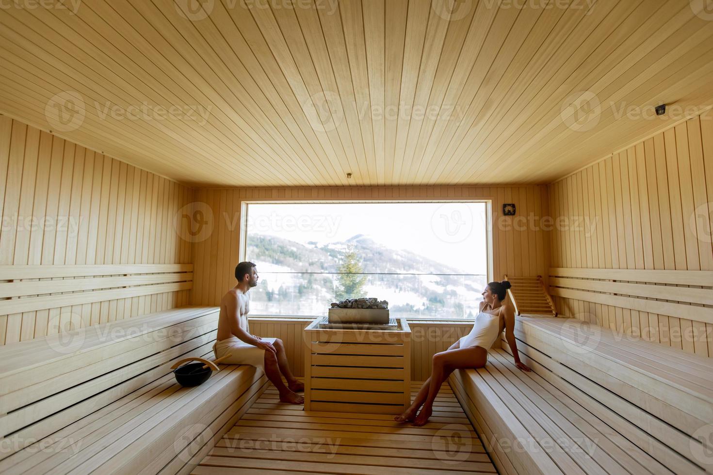 Young couple relaxing in the sauna and watching winter forest through the window photo