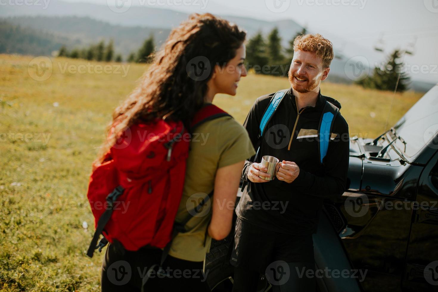 pareja joven relajándose en el capó de un vehículo todoterreno en el campo foto