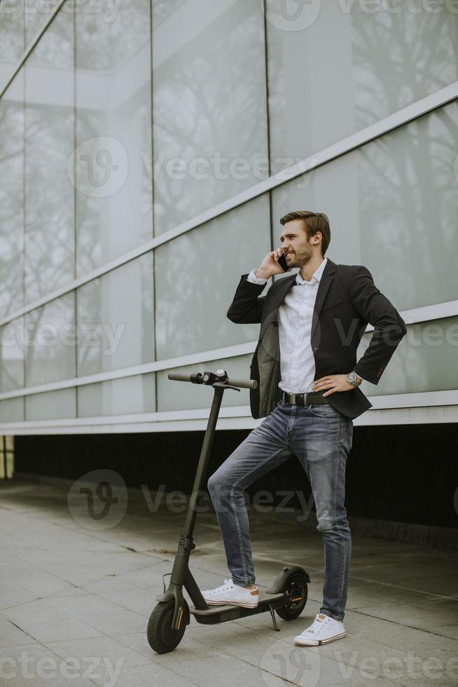 Young businessman using mobile phone  on electric scooter photo