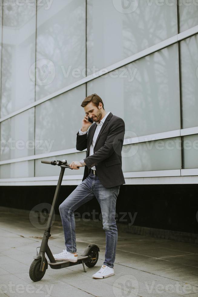 Joven empresario mediante teléfono móvil en scooter eléctrico foto