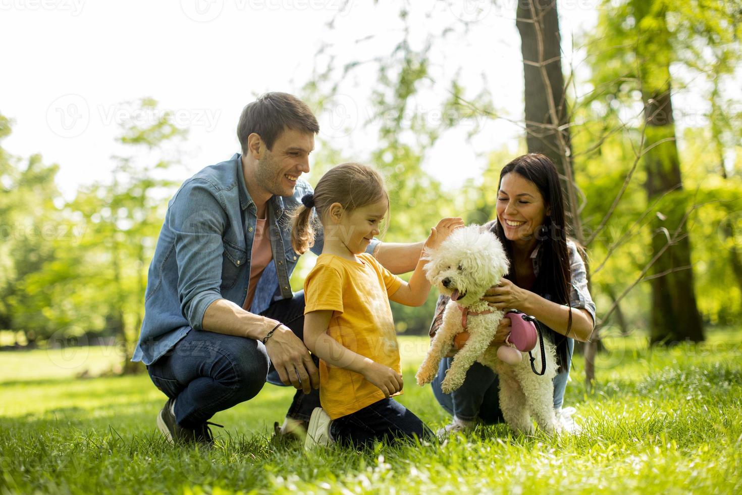 hermosa familia feliz se está divirtiendo con el perro bichon al aire libre foto