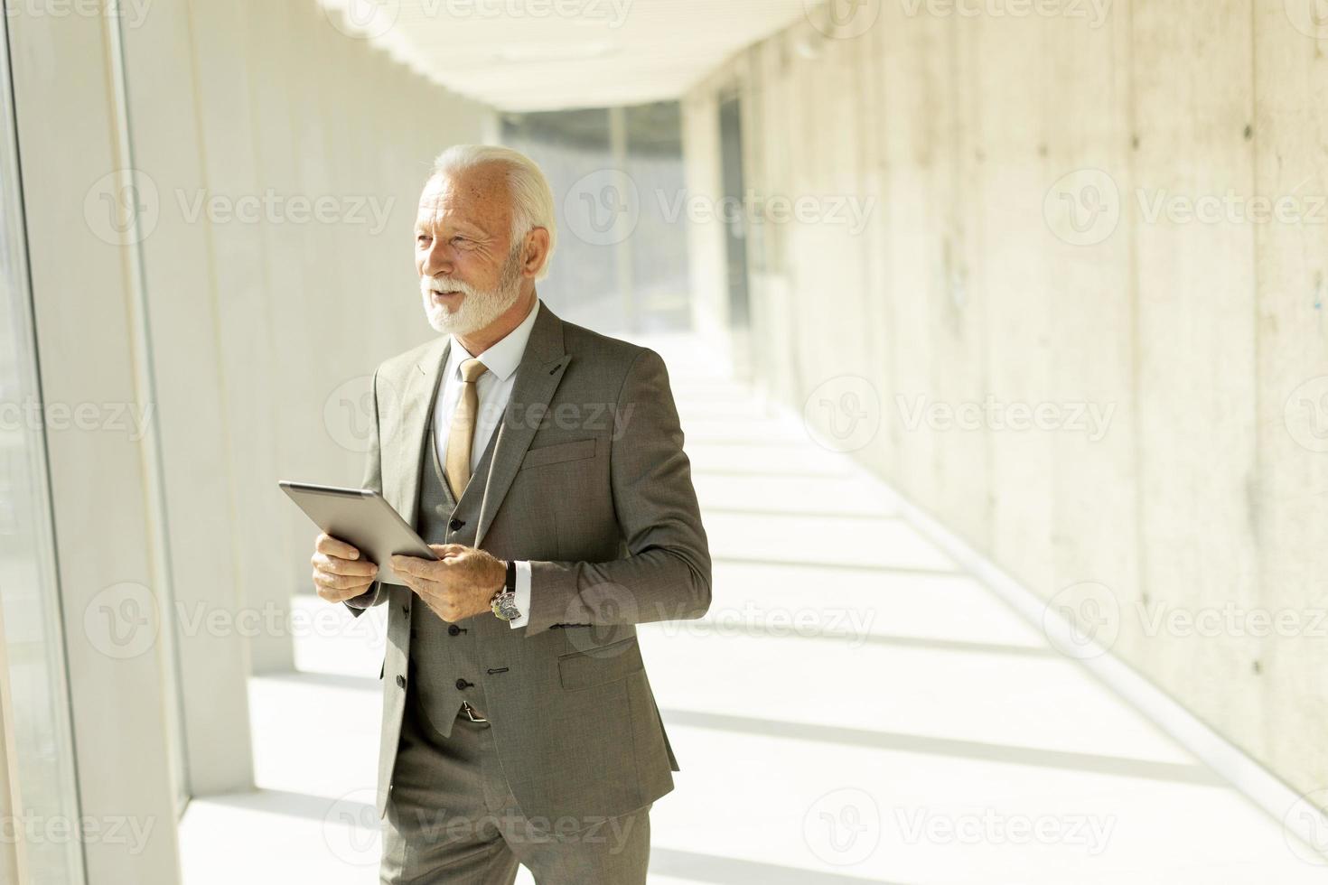 Mature businessman standing with digital tablet in the office corridor photo