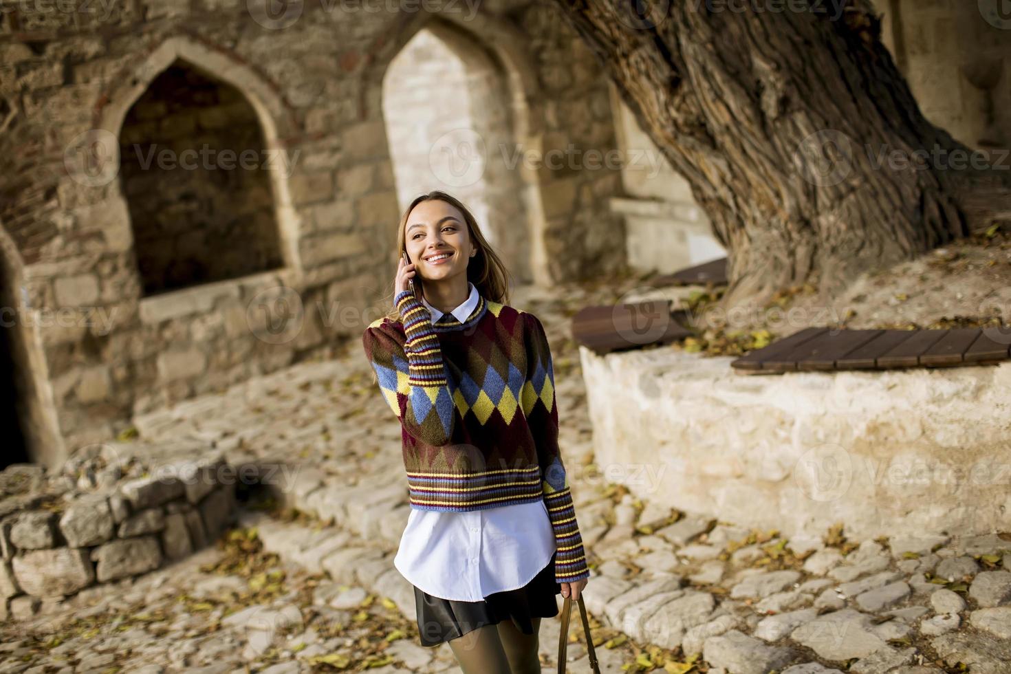 Pretty young woman walking in autumn park and using a mobile phone photo
