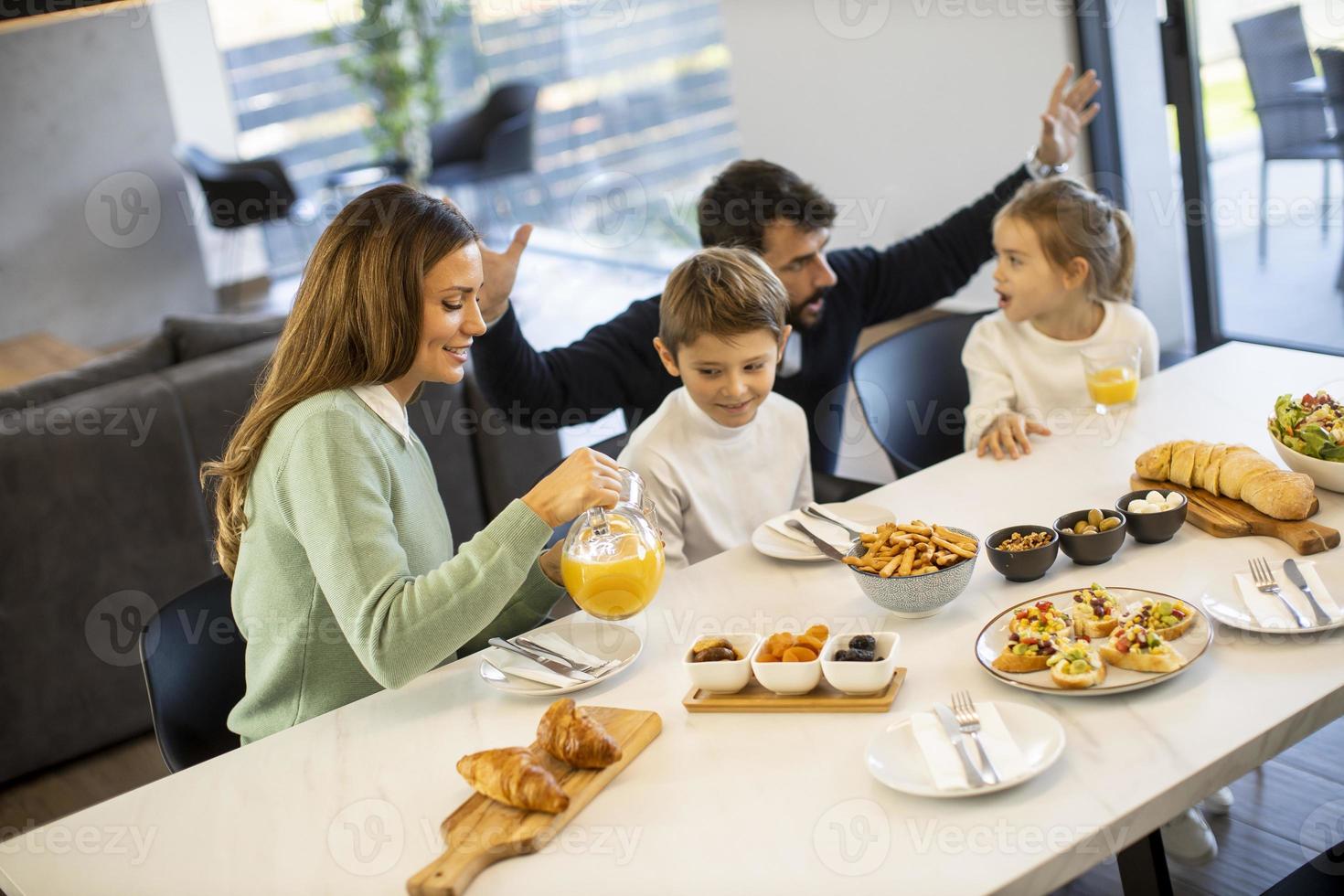 Young happy family talking while having breakfast at dining table photo