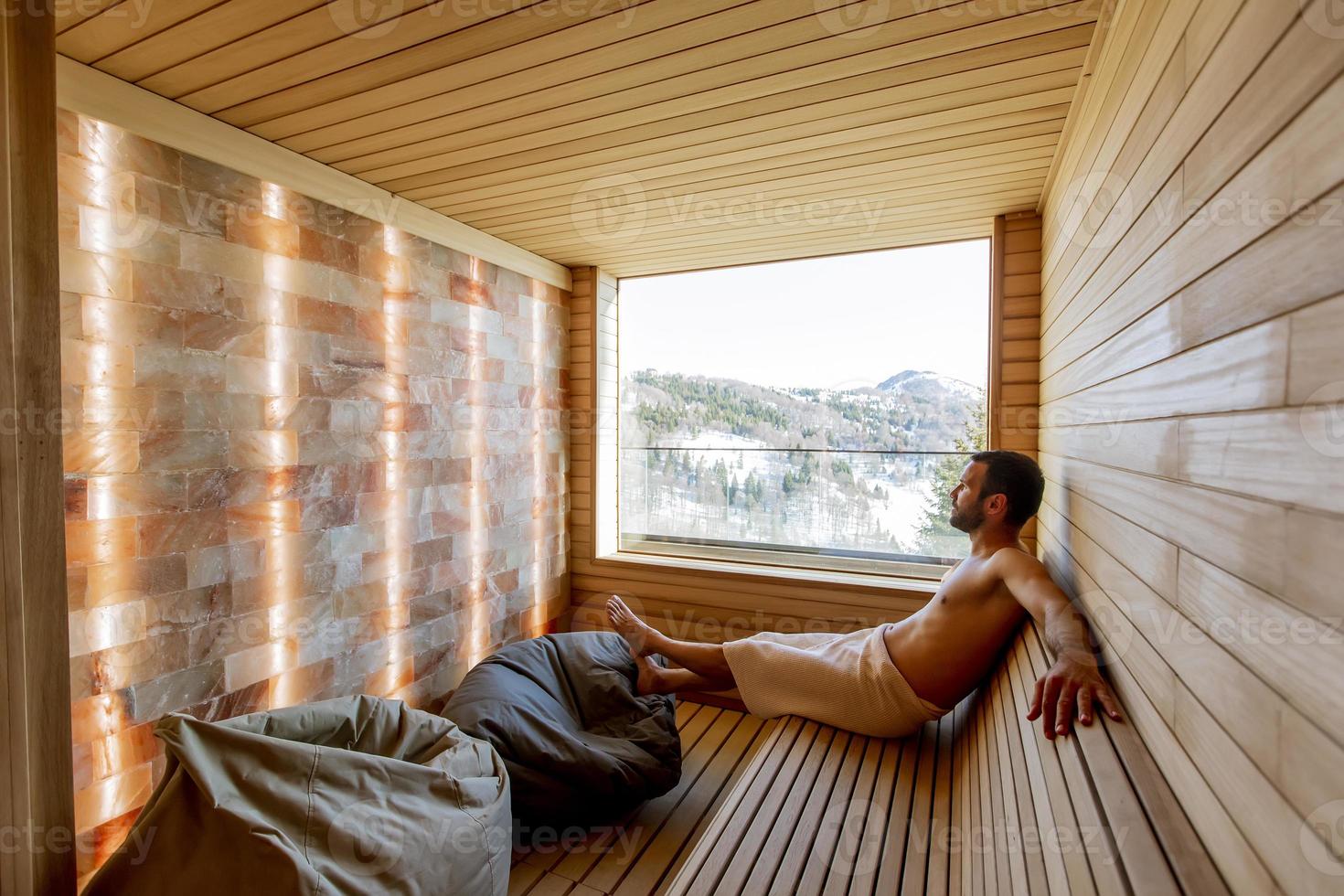 Young man relaxing in the sauna and watching winter forest through the window photo