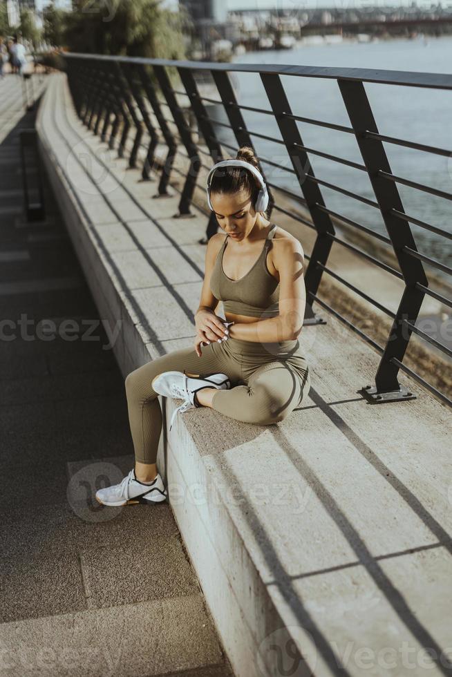Pretty young woman with earphones takes a break after running in urban area photo