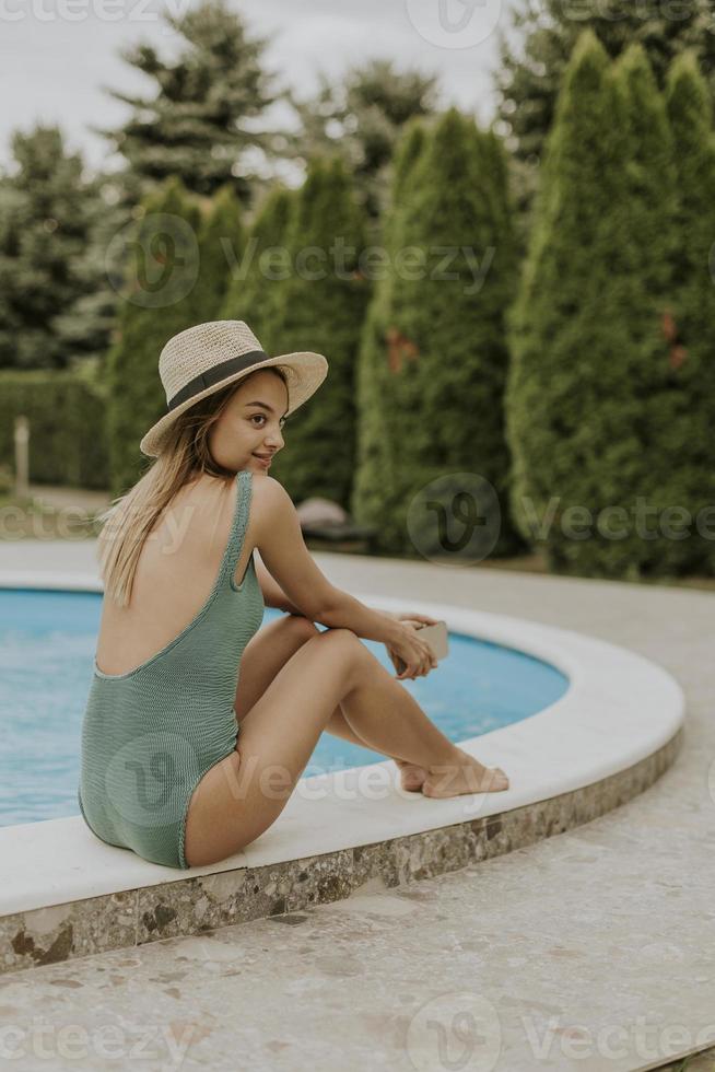 Young woman sitting by the swimming pool with mobile phone  in the house backyard photo