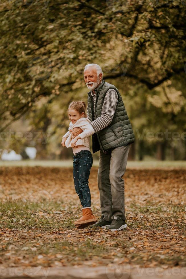 Grandfather spending time with his granddaughter in park on autumn day photo