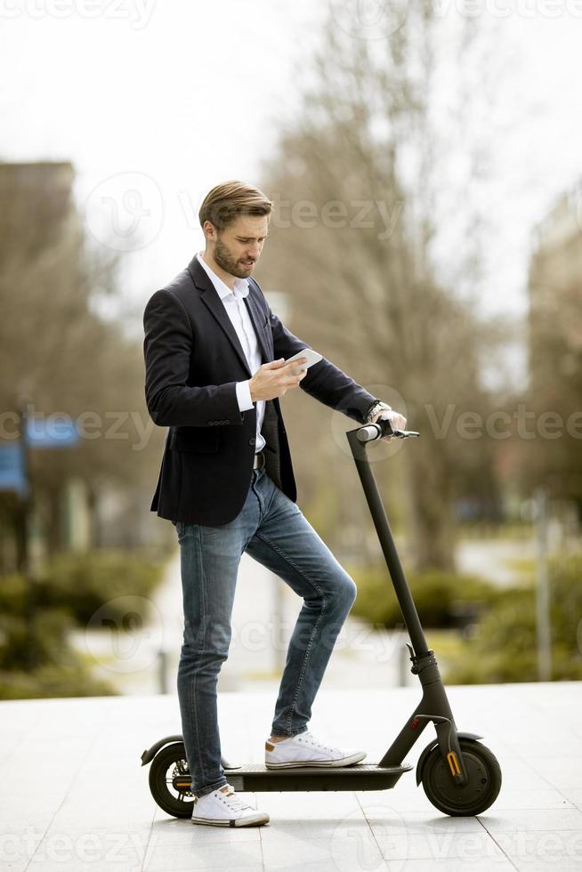 Joven empresario mediante teléfono móvil en scooter eléctrico foto