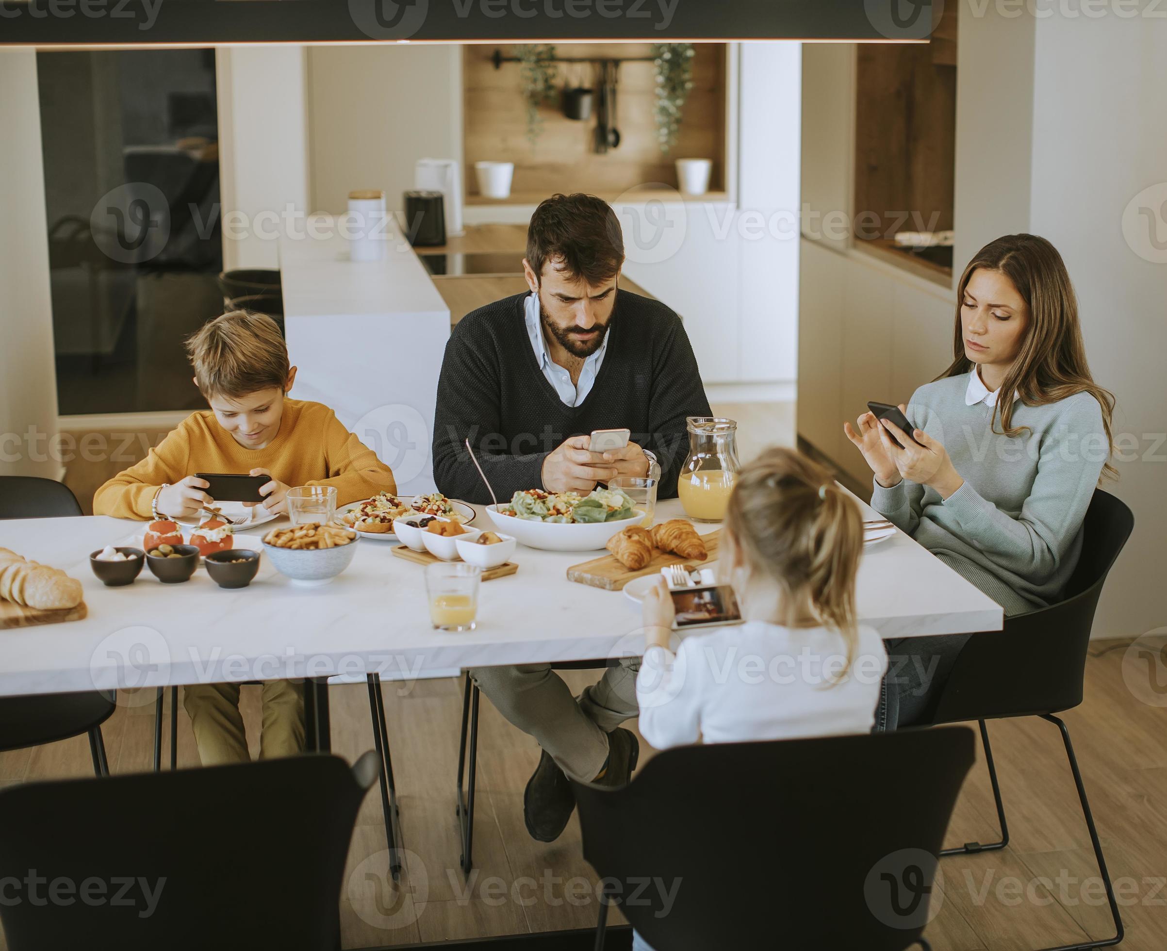 Family using mobile phones while having breakfast at dining table at ...