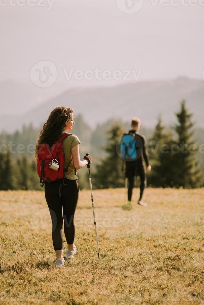 Smiling couple walking with backpacks over green hills photo