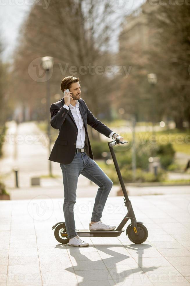 Young businessman using mobile phone  on electric scooter photo