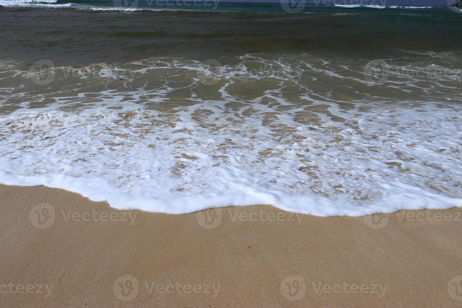 orilla del océano con playa de arena y olas que avanzan. espuma de agua con arena suave. hermosas olas en el fondo de la playa de arena. foto