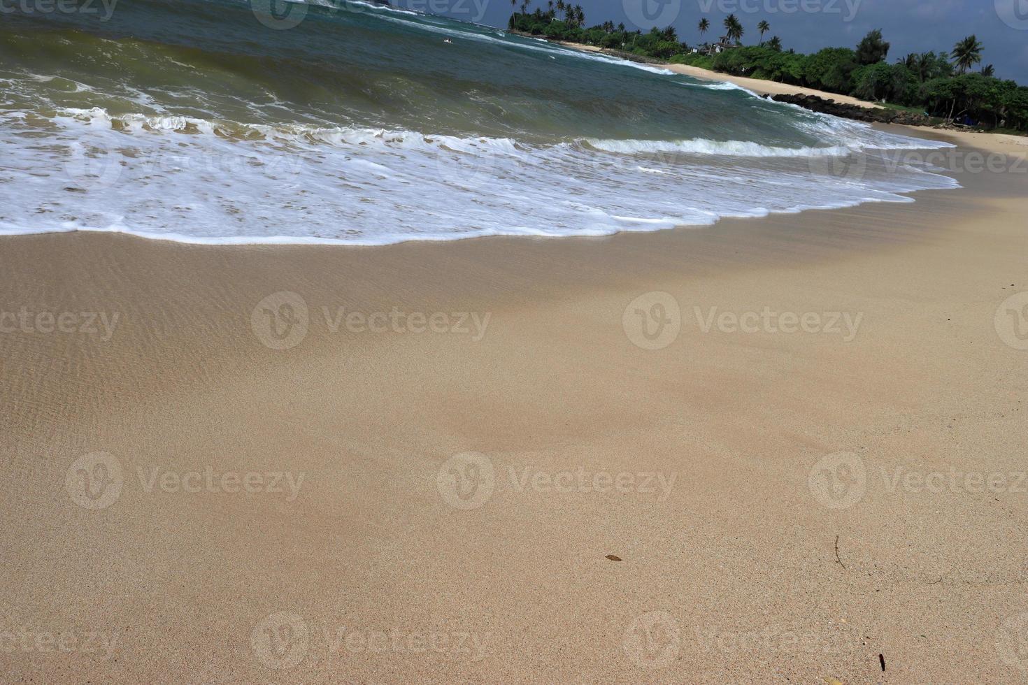 Ocean shore with sandy beach and advancing wave.  Water foam with smooth sand.  Beautiful waves on the sand beach background. photo