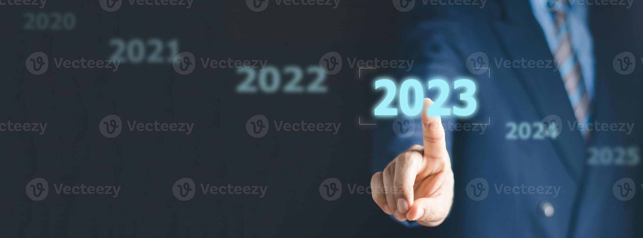 Businessman pressing 2023 start up business. Beginning of New Year 2023.Finger pressing blue start 2023 button on virtual interface on gray background with copy space for text. Concept of new year. photo