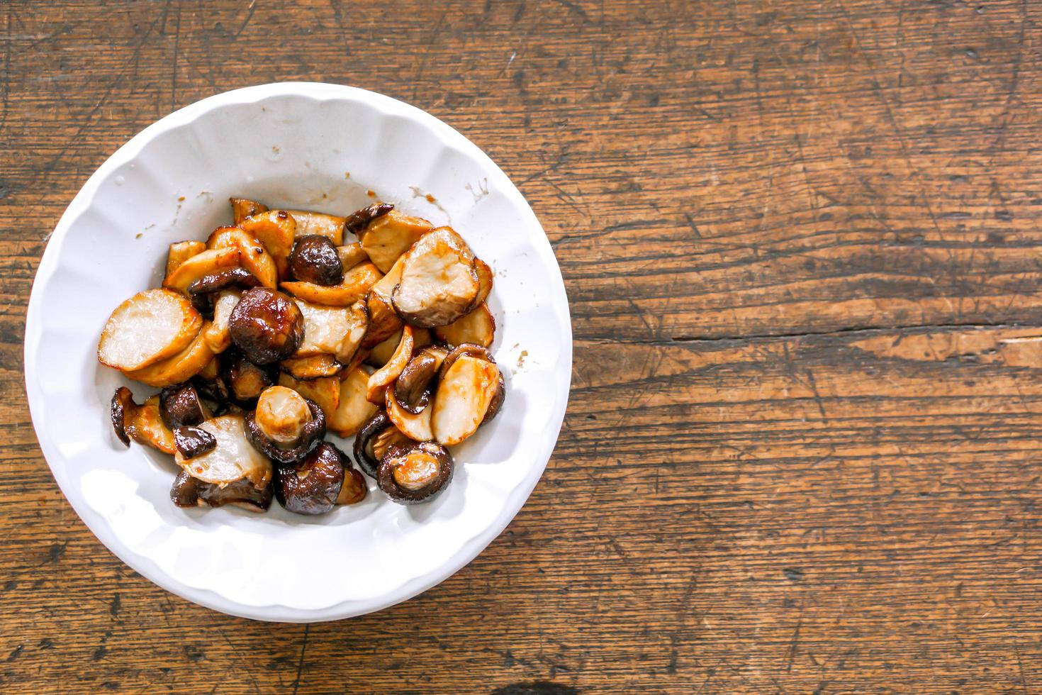 champiñones shiitake frescos salteados con salsa de soja al estilo chino sobre plato de cerámica blanca y fondo de madera. una comida vegetariana en el festival vegetariano chino. foto