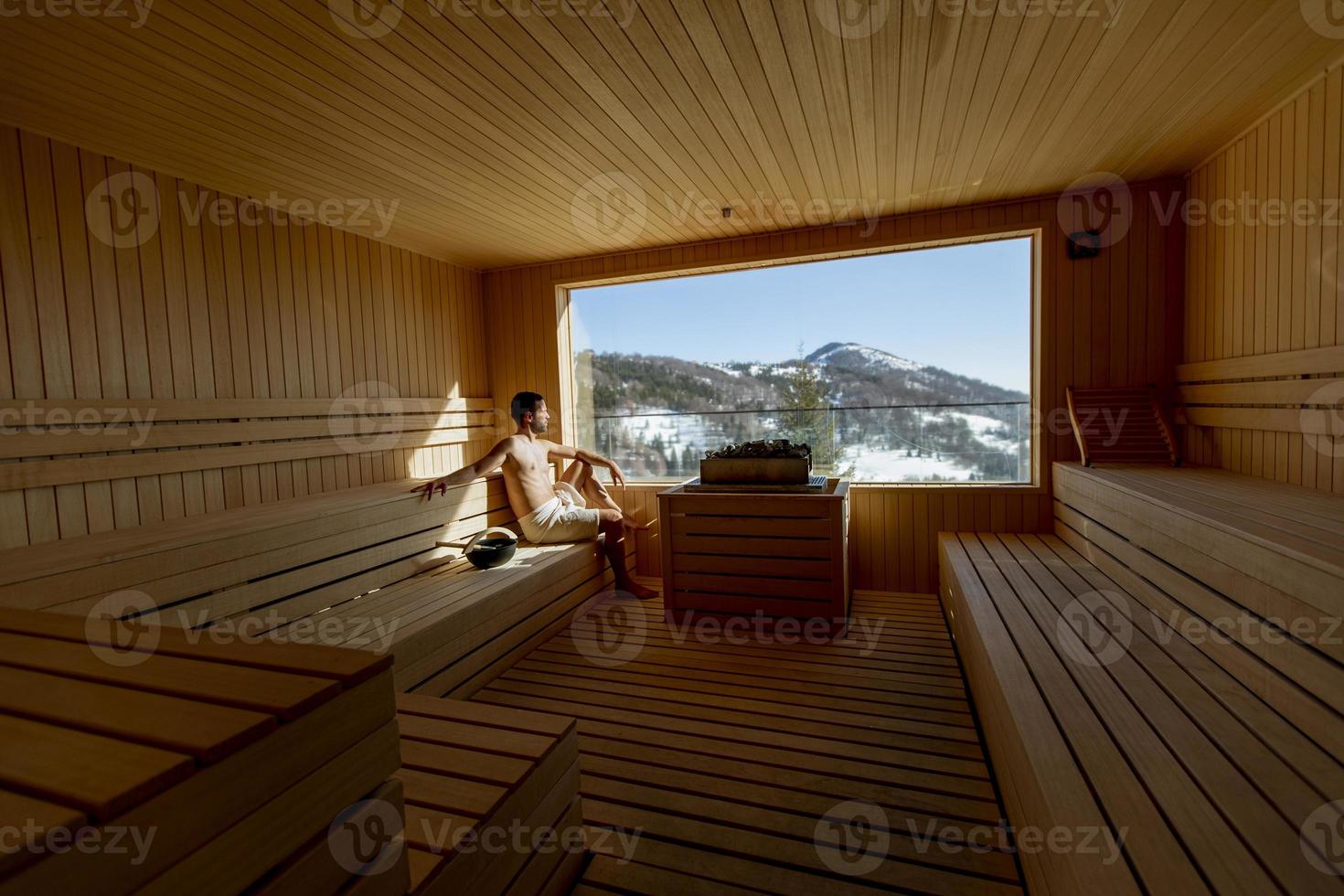 Young man relaxing in the sauna and watching winter forest through the window photo